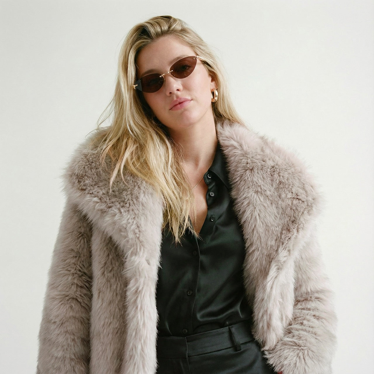 Woman wearing a fur coat and sunglasses against a white background
